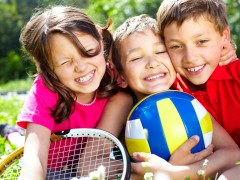 Three children with sports equipment embracing, looking at camera and smiling