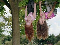Two girls (8-10) hanging upside down in tree, smiling, portrait